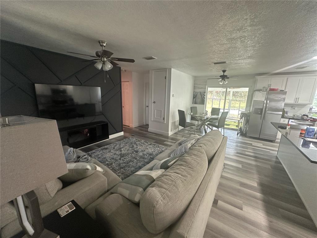 An open-concept living room and kitchen feature gray wood-look flooring and a dark accent wall — 1011 GERONA AVENUE, DELTONA, FL
