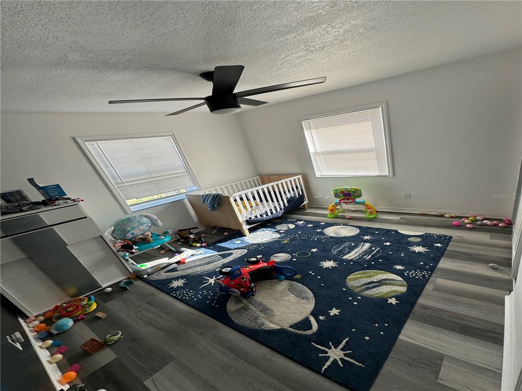 A nursery features a space-themed rug, a crib, and light-colored wood-look flooring — 1011 GERONA AVENUE, DELTONA, FL