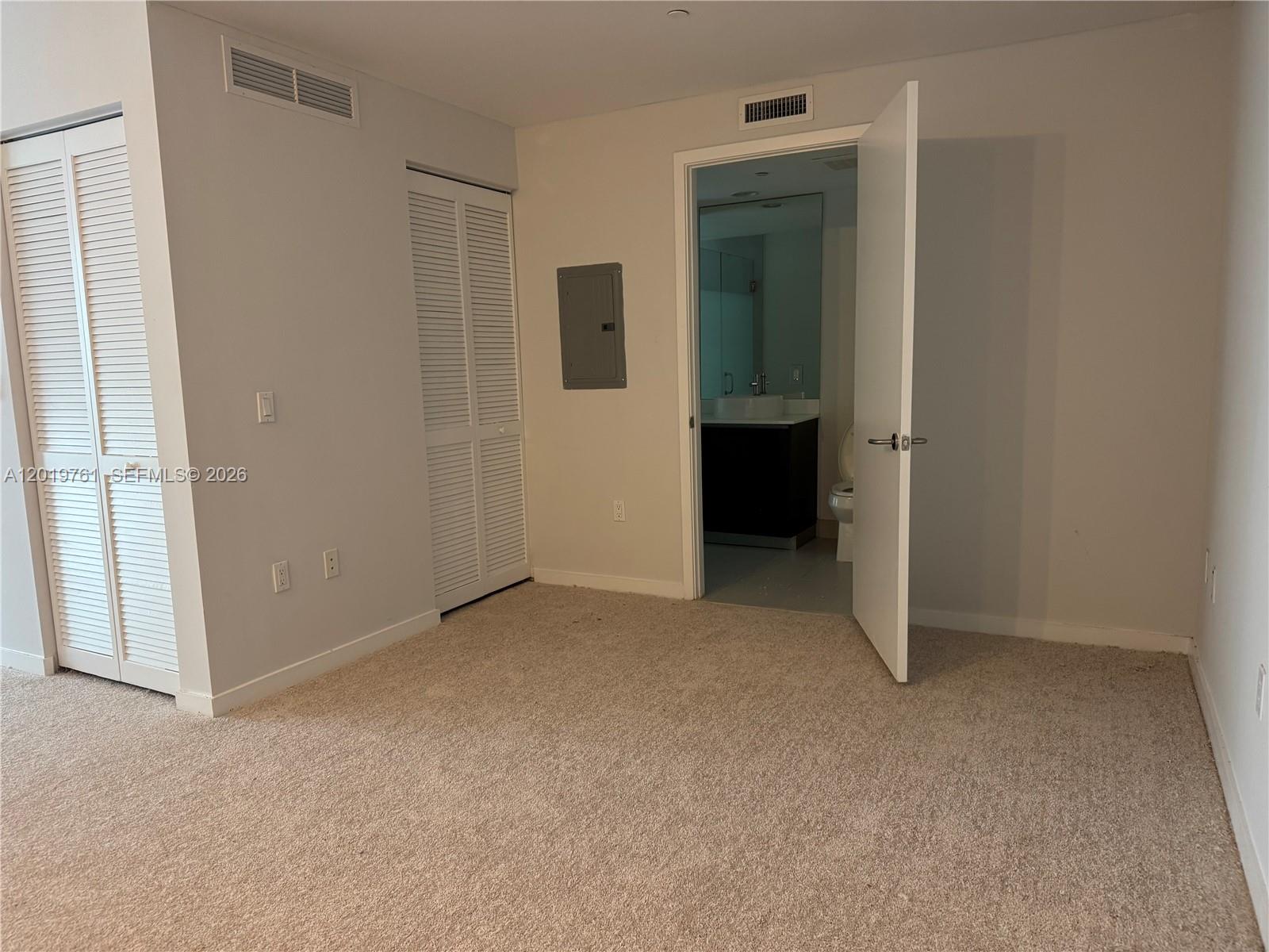 A bedroom features beige carpeting, two louvered closet doors, and an open doorway to a bathroom — 31 SE 6th St # 2004, Miami FL 33131, MIAMI, FL
