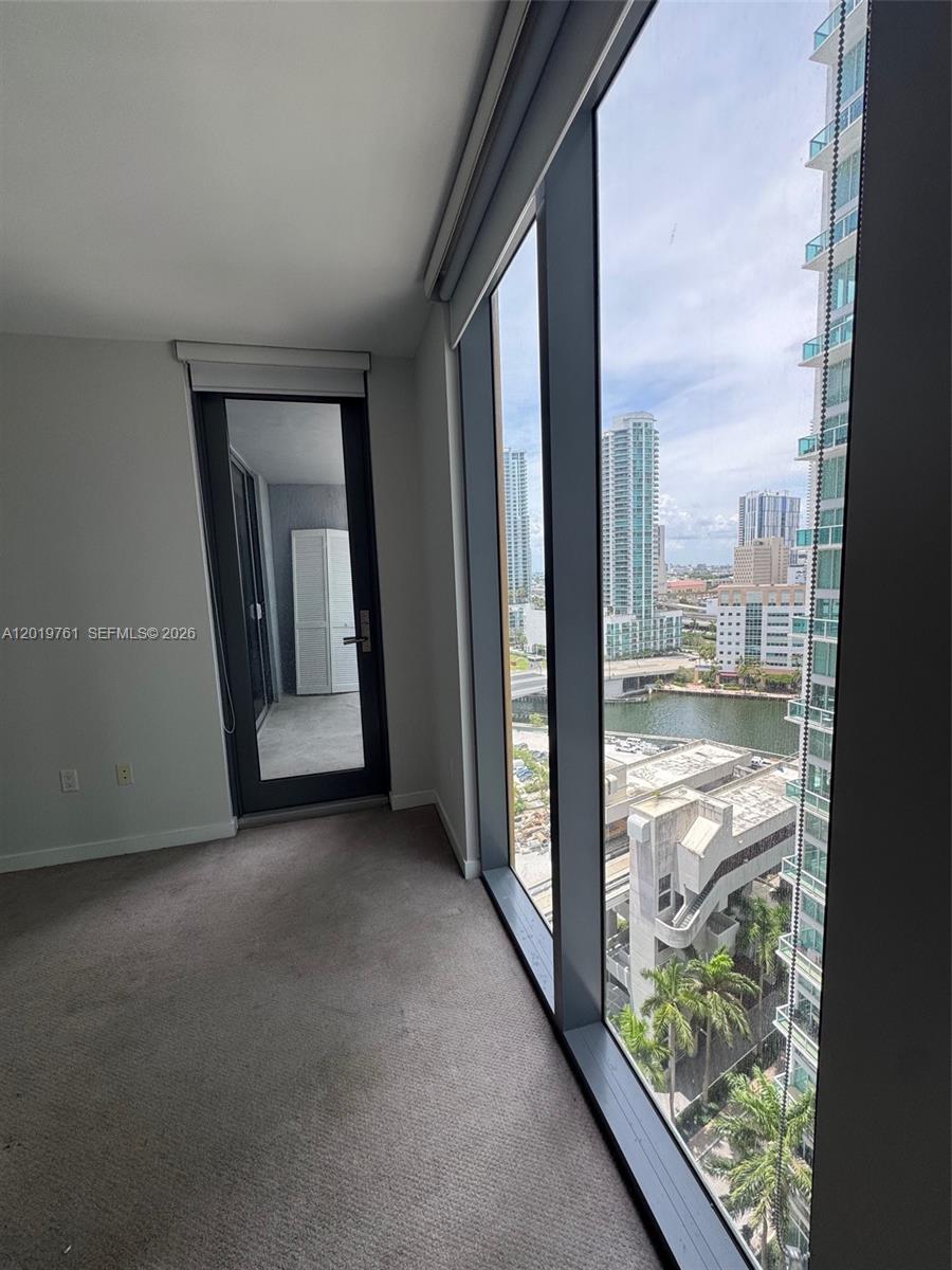 A carpeted room features floor-to-ceiling windows with a city and water view and a balcony — 31 SE 6th St # 2004, Miami FL 33131, MIAMI, FL
