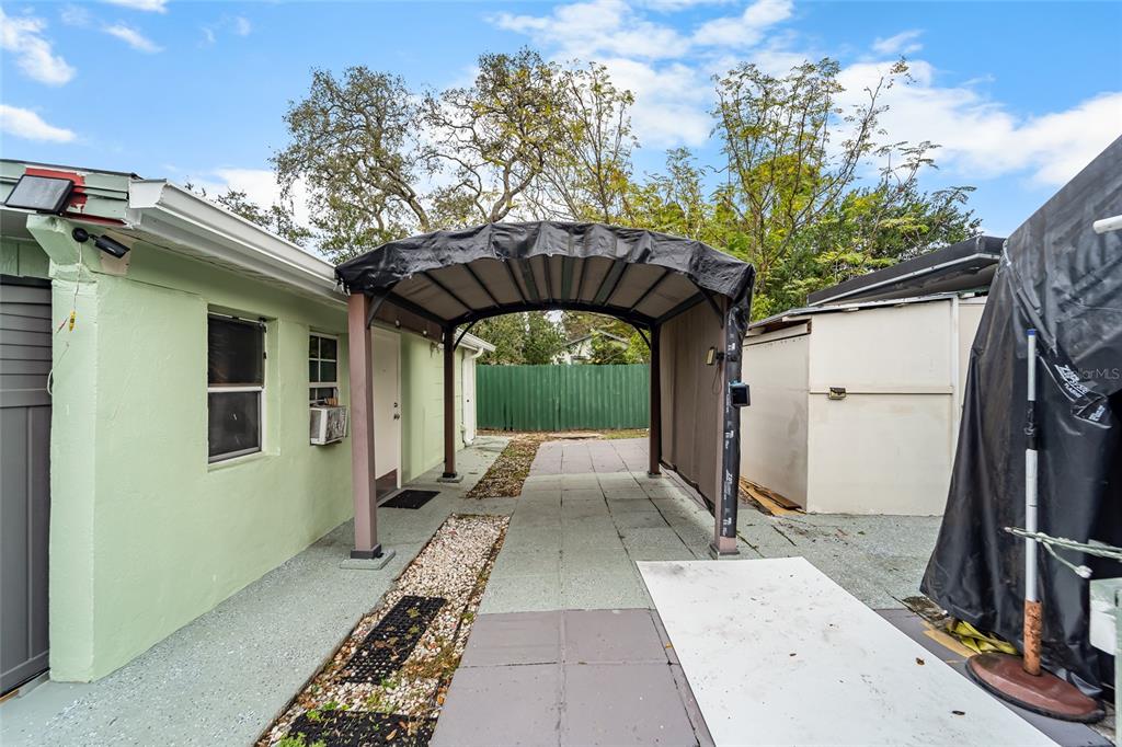 An outdoor carport with a metal frame sits between a light green building and a shed — 10001 N ARDEN AVENUE, TAMPA, FL
