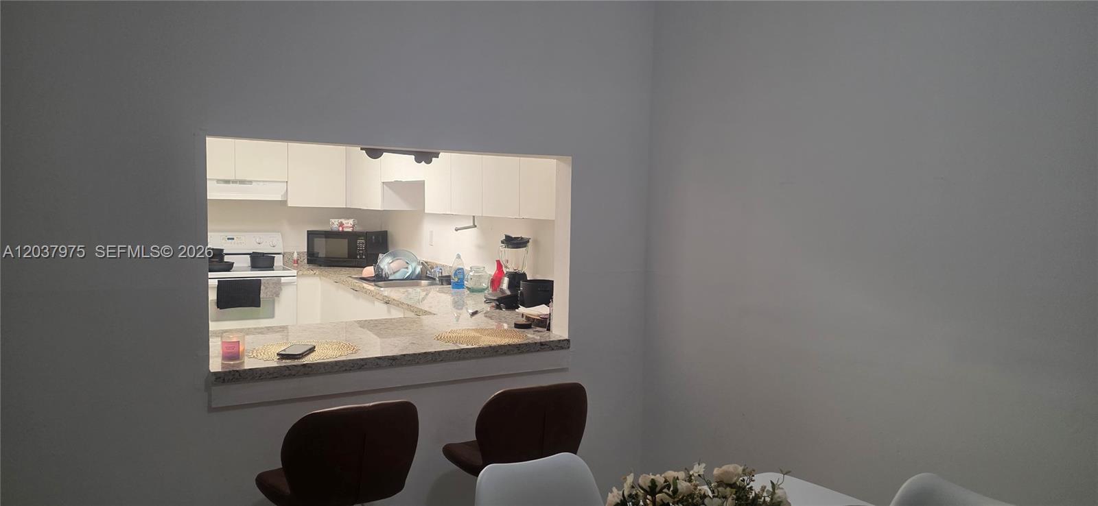 A kitchen with white cabinets and granite countertops is visible through a pass-through window — 10000 NW 80th Ct # 2149, Hialeah Gardens FL 33016, HIALEAH GARDENS, FL