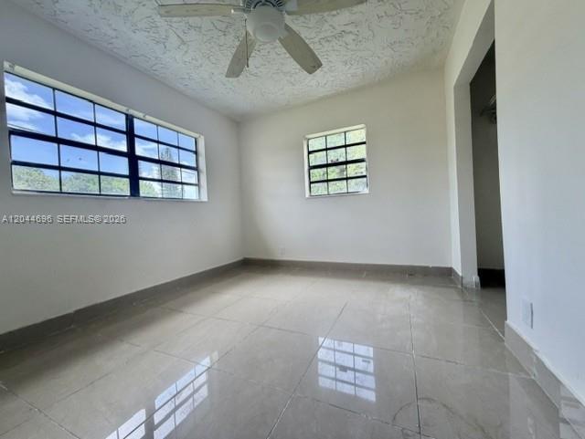An empty room features white walls, large windows, a ceiling fan, and light-colored tile flooring — 2115 SW 50th Ave, West Park FL 33023, WEST PARK, FL