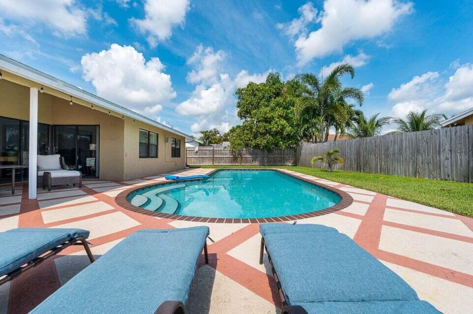 A backyard features a swimming pool, a concrete patio with geometric patterns, and lounge chairs — 9102 Bedford Drive, Boca Raton FL 33434, BOCA RATON, FL