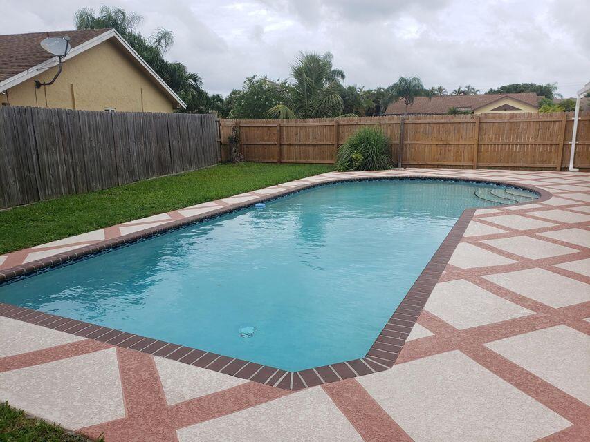 A backyard features a rectangular swimming pool with a decorative paver deck and wooden fencing — 9102 Bedford Drive, Boca Raton FL 33434, BOCA RATON, FL