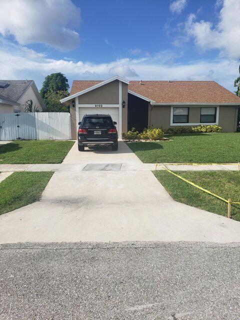 A single-story house with a tan exterior, brown roof, and a car parked in the driveway — 9102 Bedford Drive, Boca Raton FL 33434, BOCA RATON, FL
