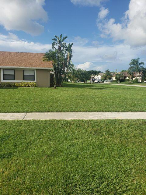 A single-story house with a tan exterior and a brown shingled roof sits beside a lawn — 9102 Bedford Drive, Boca Raton FL 33434, BOCA RATON, FL