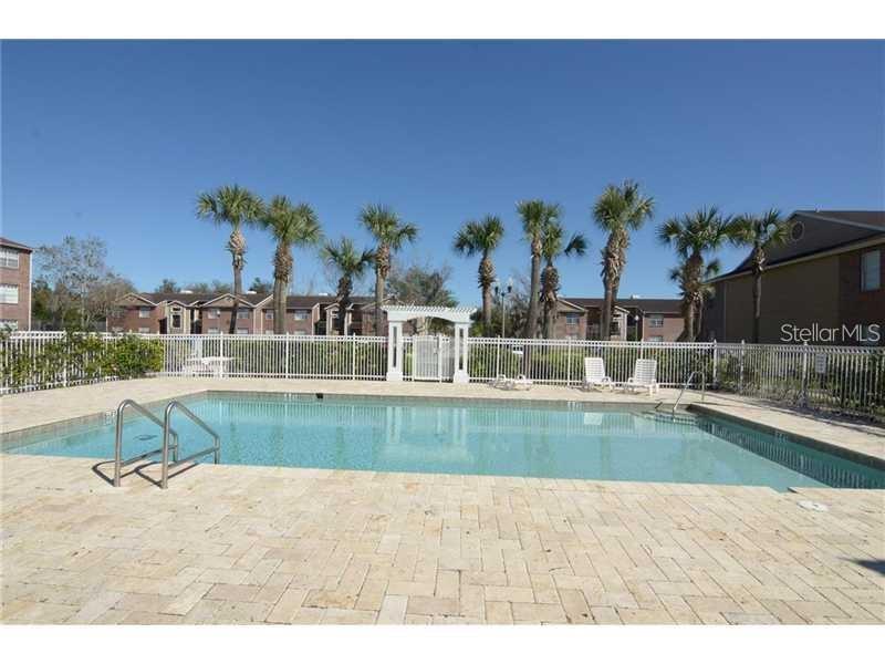 A swimming pool with a stone deck is surrounded by a white fence and palm trees — 4367 THORNBRIAR LANE UNIT P104, ORLANDO, FL