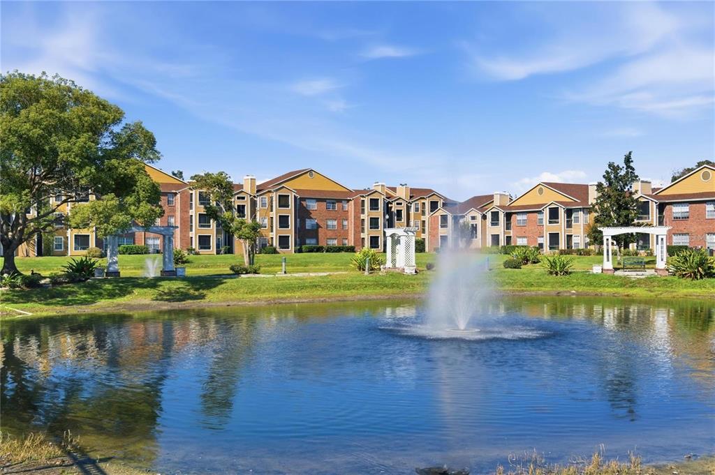 A pond with a fountain sits in front of a multi-story apartment complex — 4367 THORNBRIAR LANE UNIT P104, ORLANDO, FL