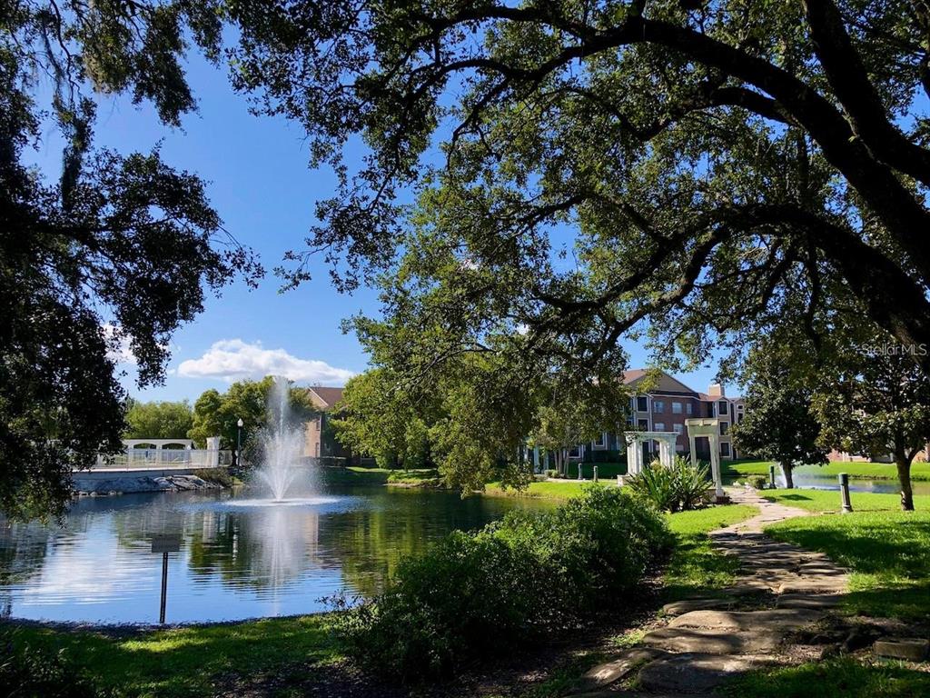 A fountain sprays water in a pond surrounded by trees, a stone path, and buildings — 4367 THORNBRIAR LANE UNIT P104, ORLANDO, FL