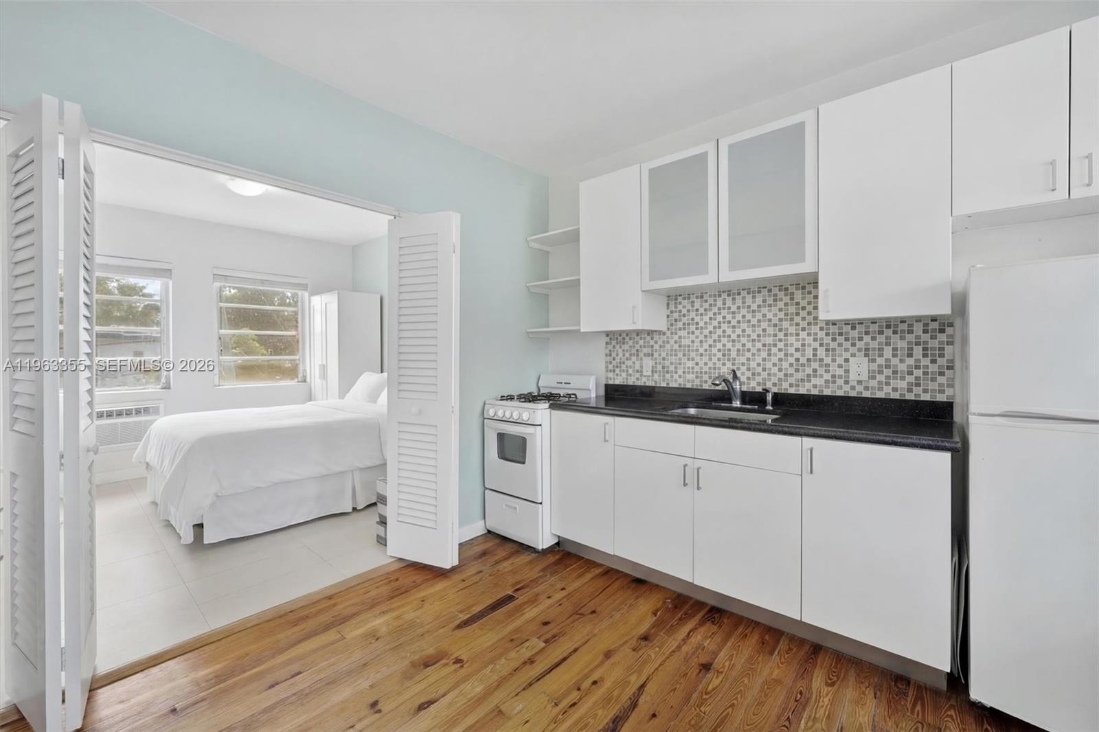 A kitchen with white cabinets and a black countertop connects to a bedroom — 1925 Washington Ave # 21, Miami Beach FL 33139, MIAMI BEACH, FL
