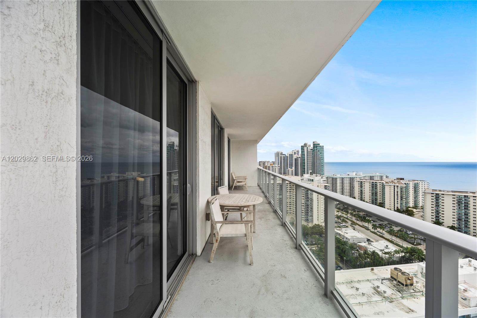 A high-rise balcony features a small wooden table, two chairs, and a glass railing — 4010 S Ocean Dr # R2307, Hollywood FL 33019, HOLLYWOOD, FL