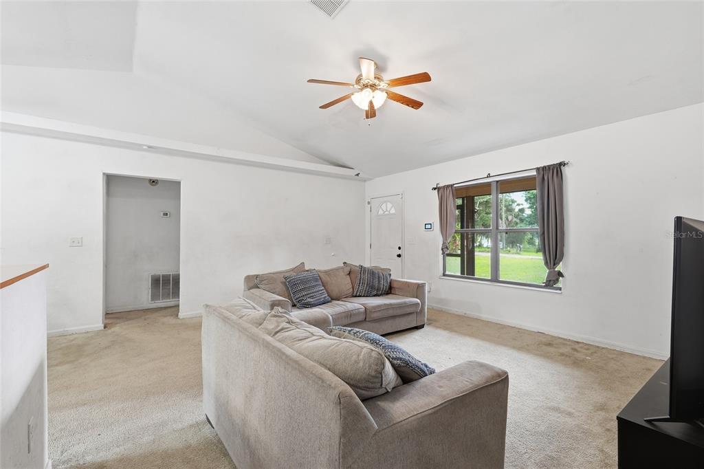 A living room with beige carpet, white walls, a ceiling fan, and two gray sofas — 173 LITTLE ORANGE LAKE DRIVE, HAWTHORNE, FL