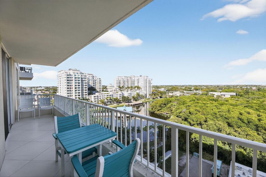 A balcony with a blue table and chairs overlooks a canal, trees, and apartment buildings — 700 E Boynton Beach Boulevard # 1006, Boynton Beach FL 33435, BOYNTON BEACH, FL