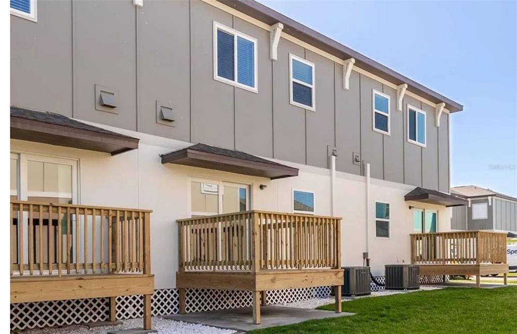 The exterior of a multi-unit townhouse features wooden decks, sliding glass doors, and gray siding — 2102 SEBRING PLACE, CLEARWATER, FL