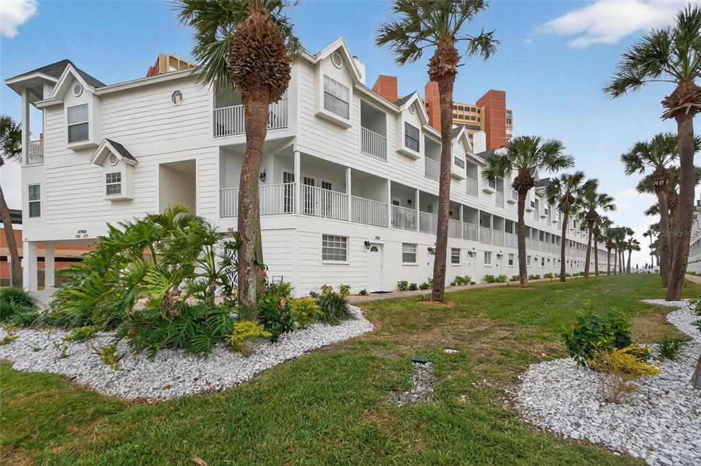 A multi-story white building with balconies and palm trees sits on a grassy lawn — 17960 GULF BOULEVARD UNIT 119, REDINGTON SHORES, FL