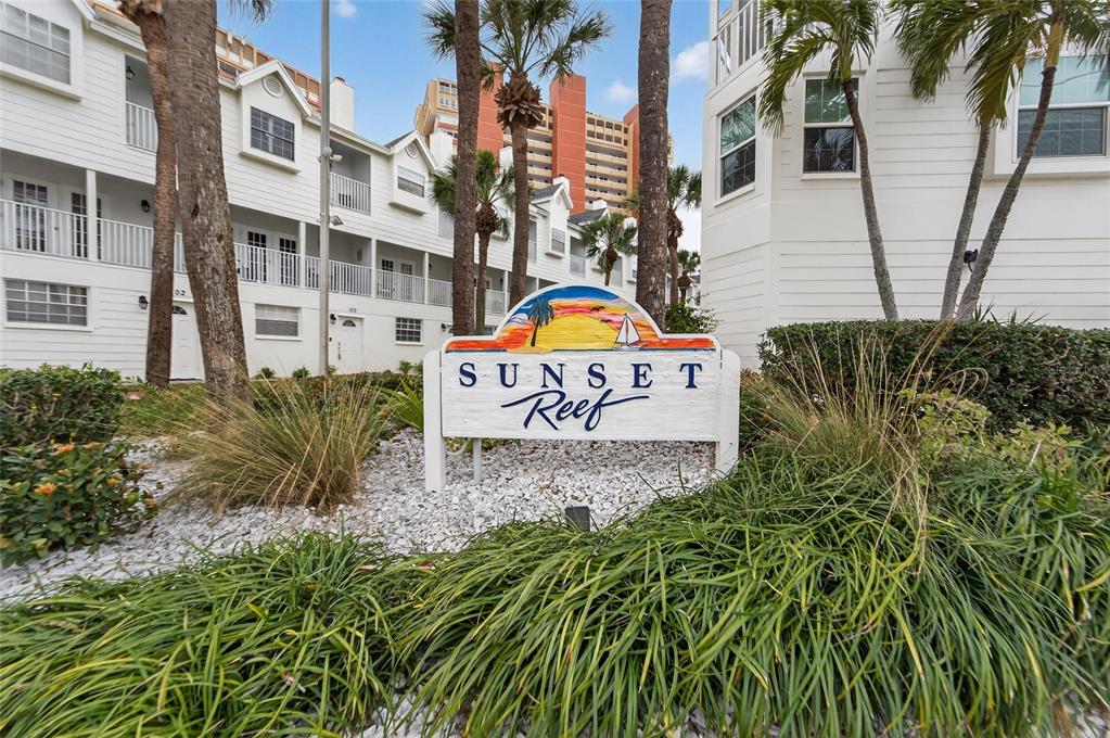 A sign for Sunset Reef stands in front of white multi-story residential buildings and palm trees — 17960 GULF BOULEVARD UNIT 119, REDINGTON SHORES, FL