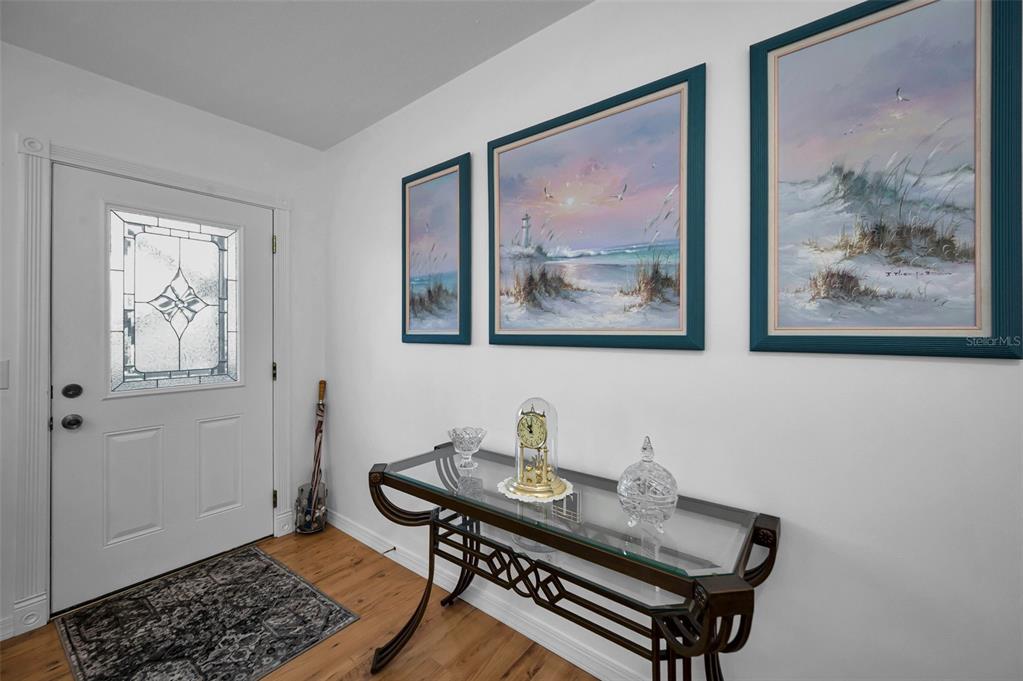 A foyer features a glass-topped console table, three coastal paintings, and a white front door — 2043 DENMARK STREET UNIT 39, CLEARWATER, FL