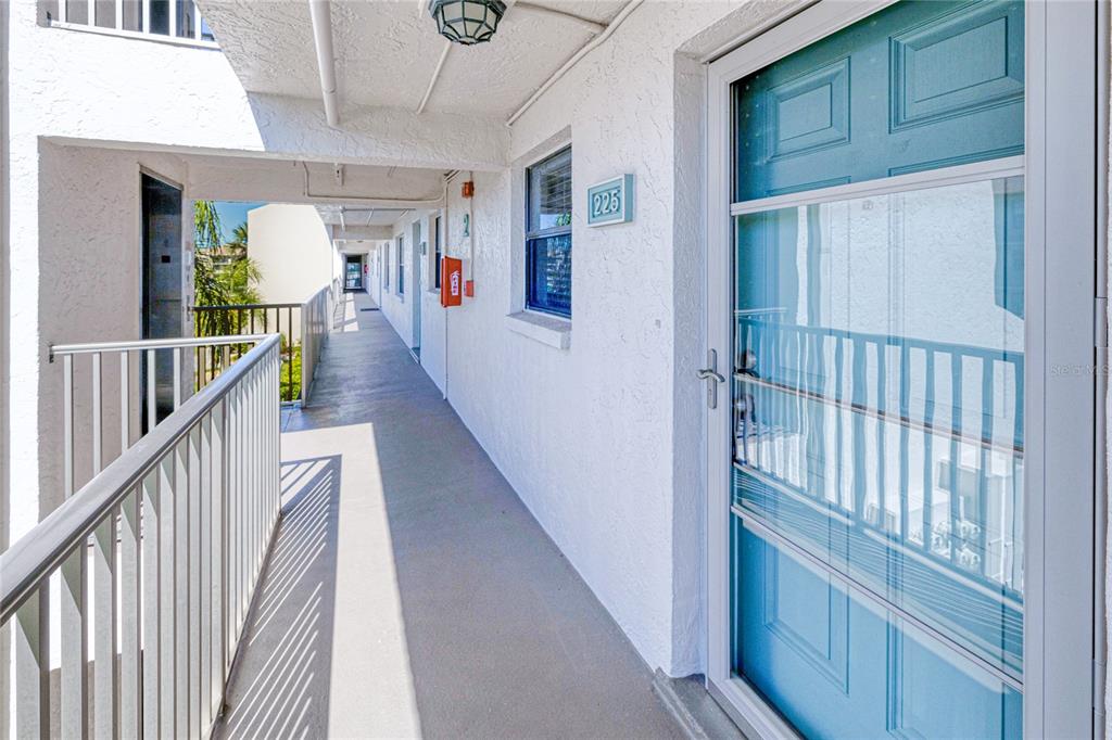 An outdoor apartment walkway features a blue door labeled 225 and a white metal railing — 175 KINGS HIGHWAY UNIT 225 (B5), PUNTA GORDA, FL
