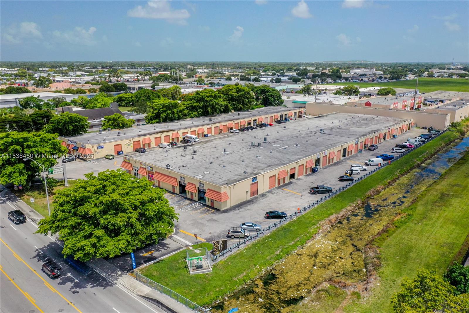 An aerial view shows a long, single-story commercial warehouse building with parking and a canal — 10890 QUAIL ROOST DR, Miami FL 33157, MIAMI, FL