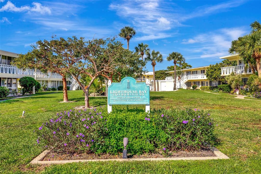 A sign for Lighthouse Bay Condominiums stands in a grassy courtyard between two-story apartment buildings — 2755 NE 28TH AVENUE UNIT A3, LIGHTHOUSE POINT, FL