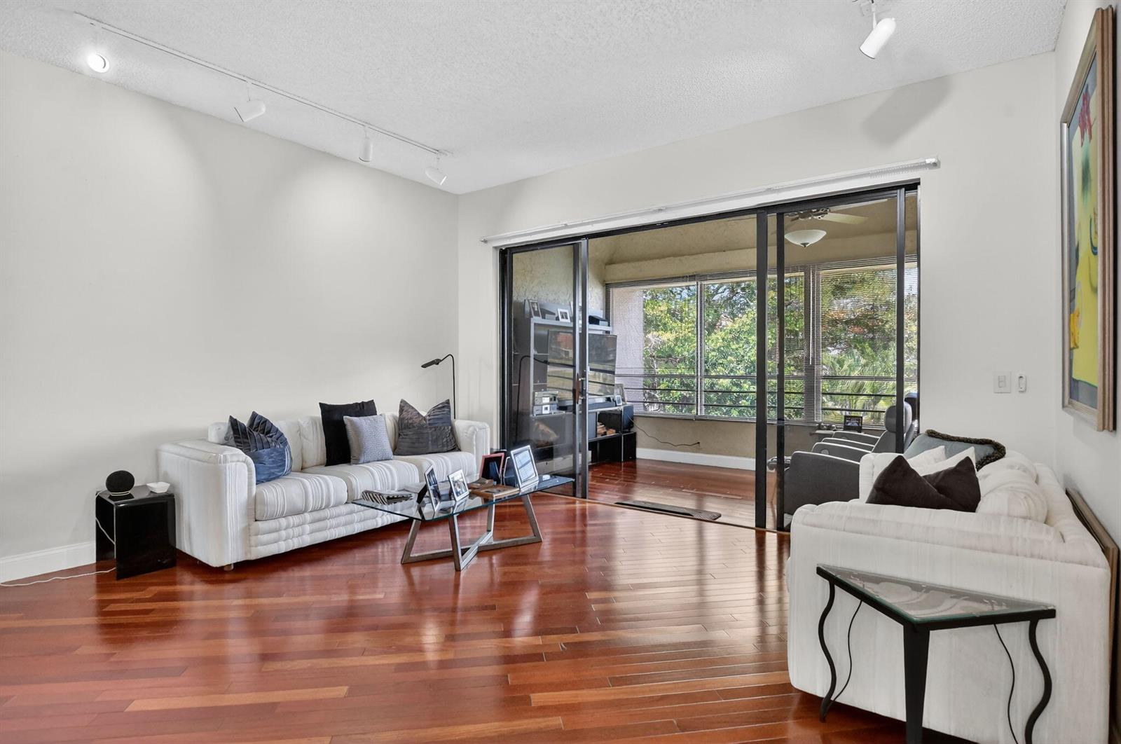 A living room with white sofas, hardwood floors, and sliding glass doors leading to a balcony — 7535 La Paz Boulevard # 301, Boca Raton FL 33433, BOCA RATON, FL