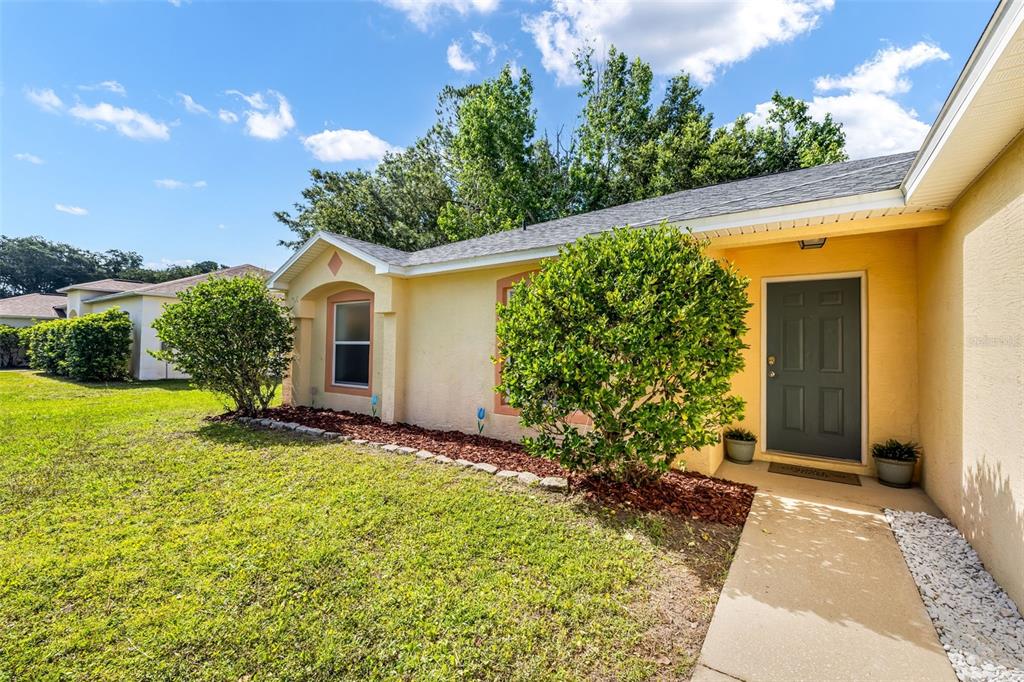 A yellow single-story house exterior features a dark front door, landscaping, and a concrete walkway — 16 SLUMBER PATH, PALM COAST, FL