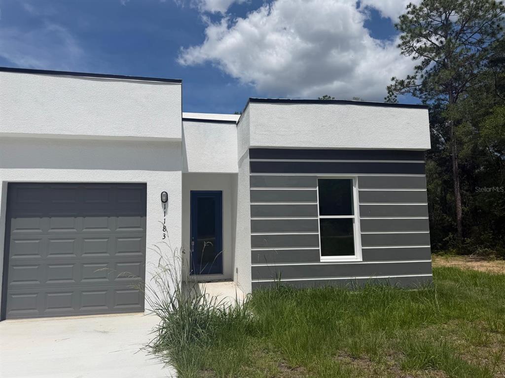 A modern, single-story house exterior features a gray garage, blue front door, and striped siding — 11183 N VESTA POINT, CITRUS SPRINGS, FL