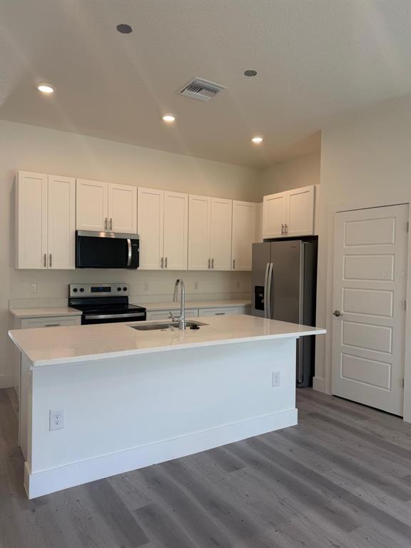 A modern kitchen features white cabinetry, stainless steel appliances, a quartz island, and gray flooring — 11183 N VESTA POINT, CITRUS SPRINGS, FL