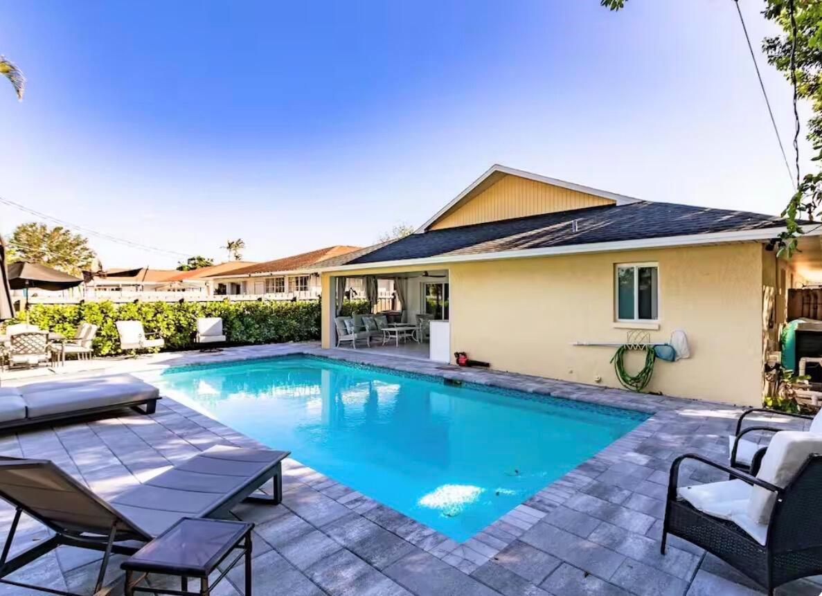 A backyard features a rectangular swimming pool, stone patio, lounge chairs, and a covered patio area — 705 N 103rd Ave Avenue N, Naples FL 34108, NAPLES, FL