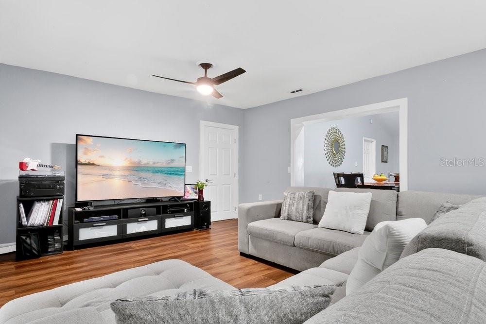 A living room features a large television, a gray sectional sofa, and wood-look flooring — 1092 W RIVIERA BOULEVARD, OVIEDO, FL