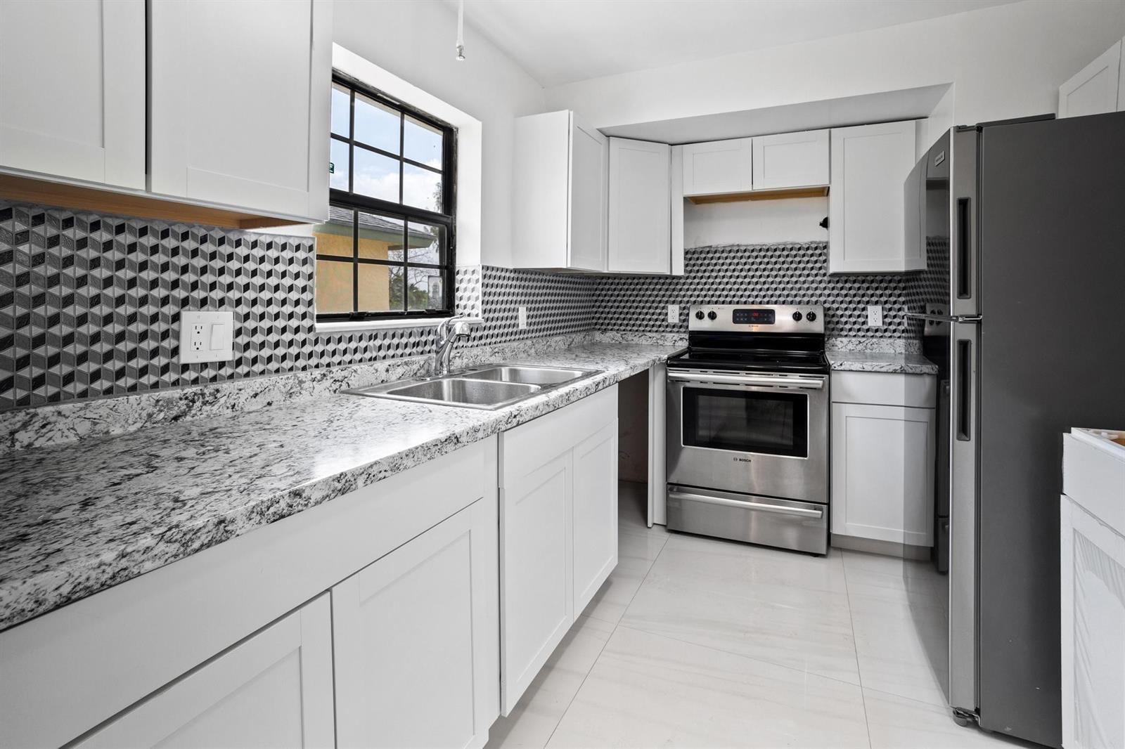 A kitchen features white cabinets, granite countertops, a geometric backsplash, and stainless steel appliances — 2355 Linton Ridge Circle # F10, Delray Beach FL 33444, DELRAY BEACH, FL