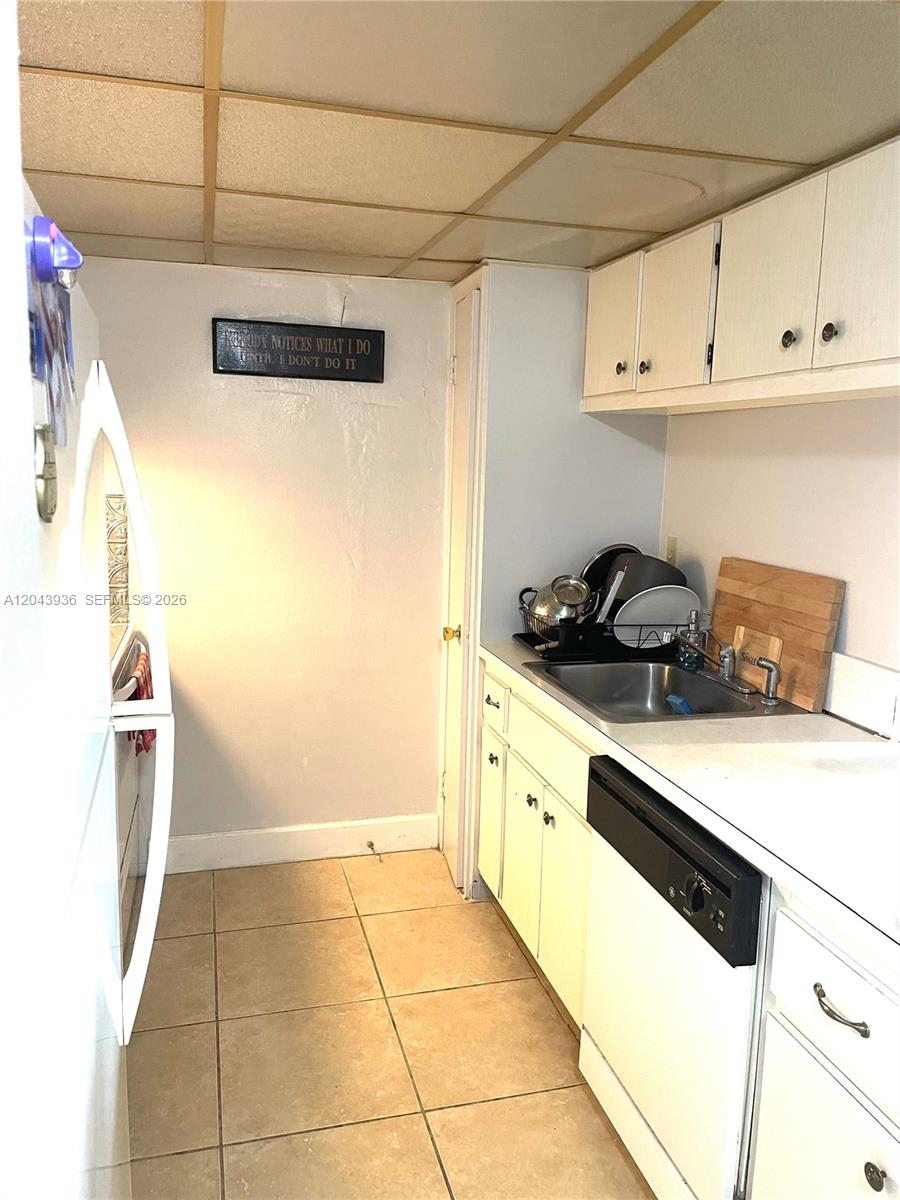 A galley kitchen features white cabinets, a stainless steel sink, and beige floor tiles — 7477 SW 82nd St # C318, Miami FL 33143, MIAMI, FL