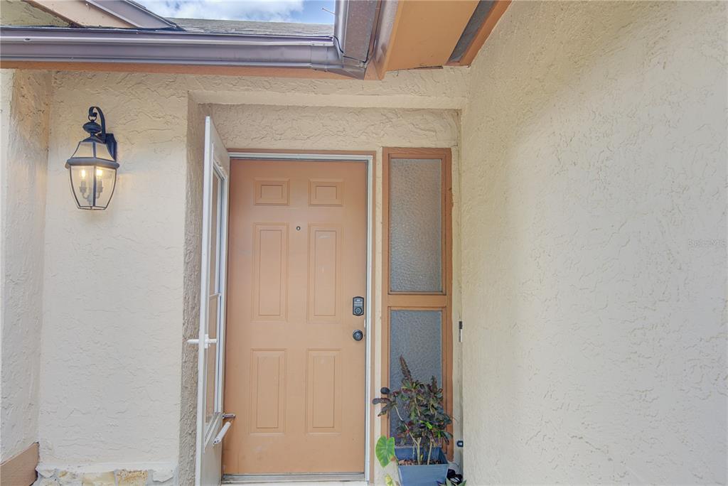 A tan front door with a side window and a wall-mounted lantern light — 1024 DINERO DRIVE, WINTER SPRINGS, FL