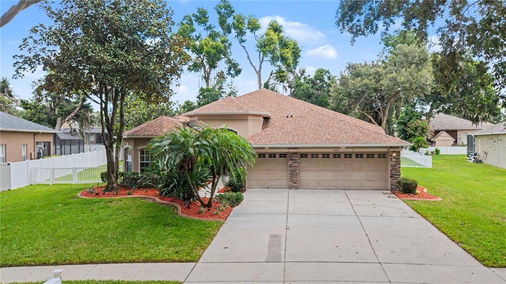 A single-story suburban house with a three-car garage, a concrete driveway, and mature landscaping — 2418 BLUE STONE COURT, VALRICO, FL