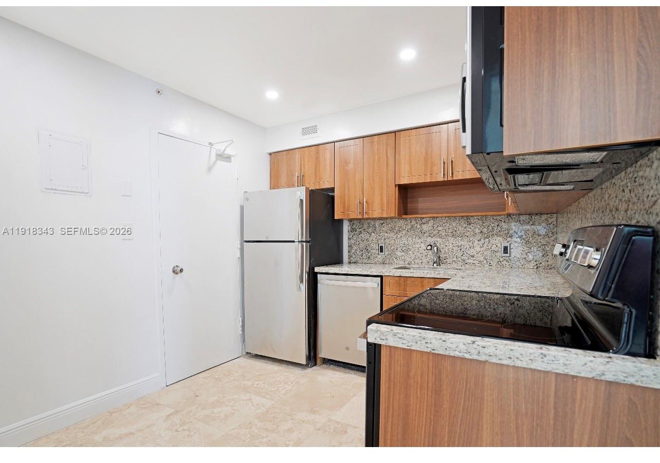 A kitchen features wood cabinets, granite countertops, stainless steel appliances, and light tile flooring — 5101 Collins Ave # 14K, Miami Beach FL 33140, MIAMI BEACH, FL