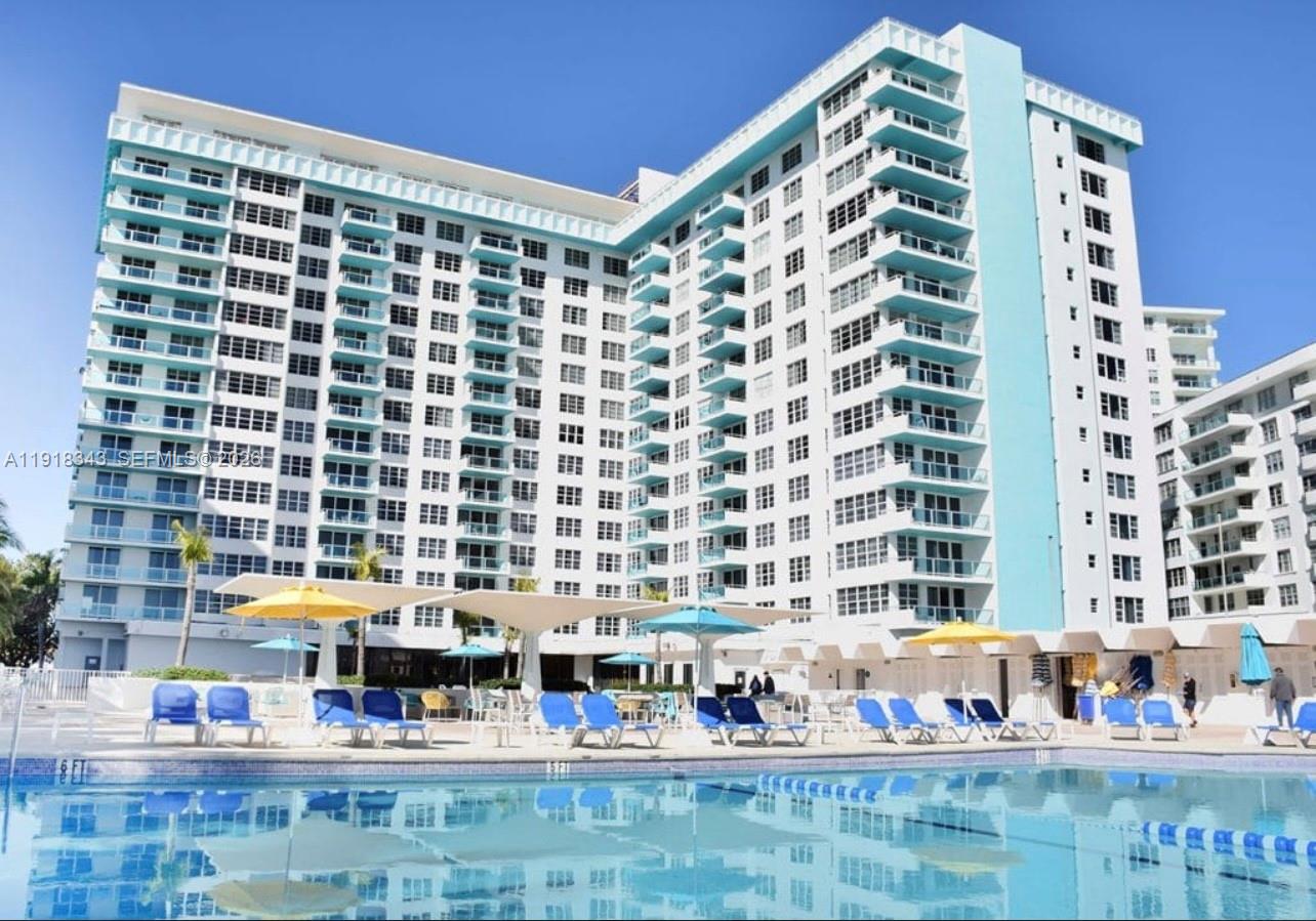 A multi-story white apartment building with blue balconies overlooks a swimming pool and patio — 5101 Collins Ave # 14K, Miami Beach FL 33140, MIAMI BEACH, FL