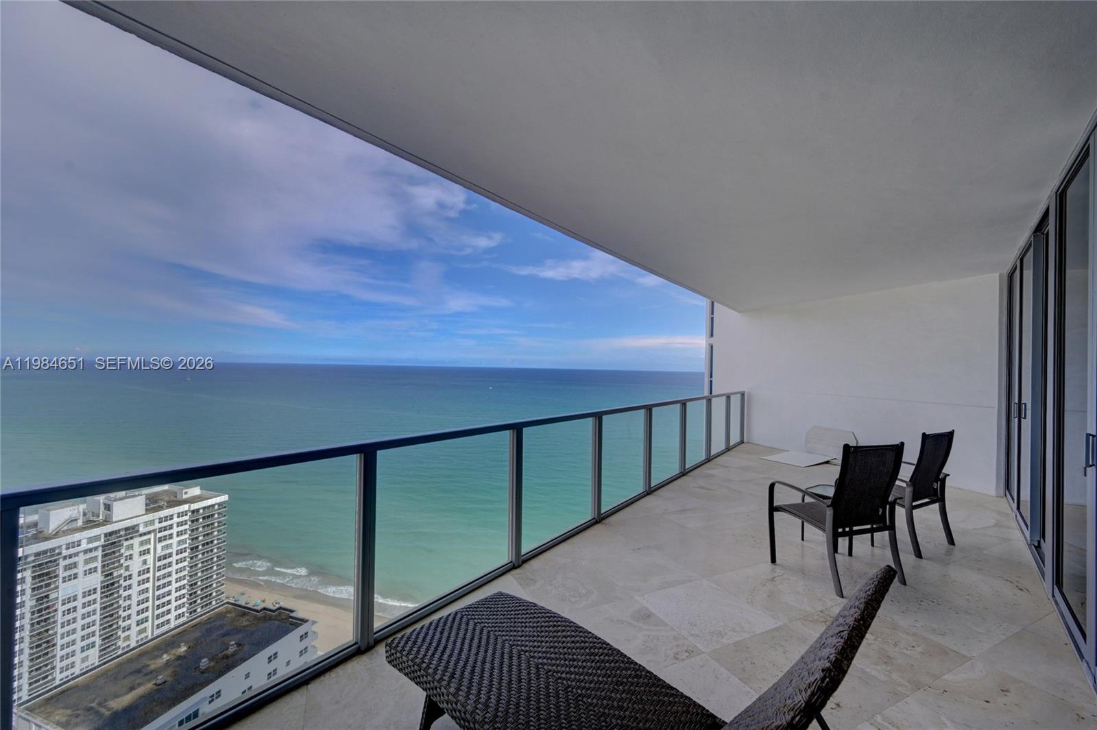 A balcony with tile flooring overlooks the ocean and a neighboring high-rise building — 3101 S Ocean Dr # 3203, Hollywood FL 33019, HOLLYWOOD, FL