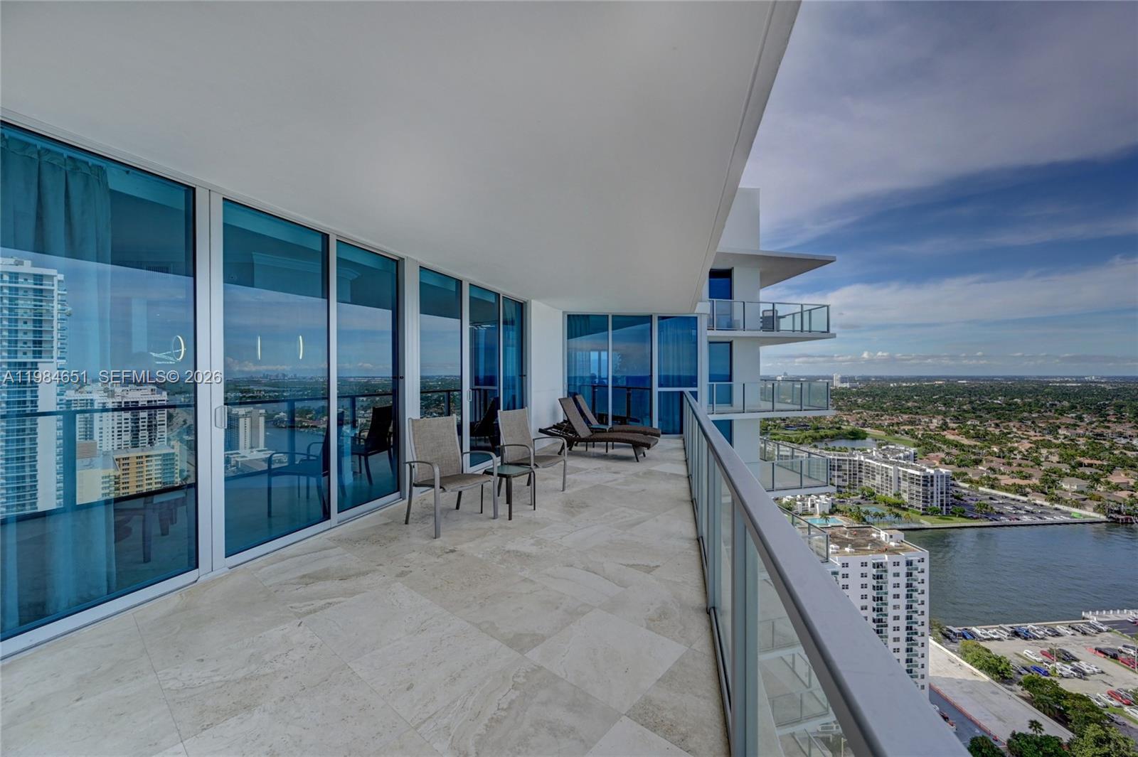 A high-rise balcony features tile flooring, glass railings, and outdoor furniture overlooking a city waterway — 3101 S Ocean Dr # 3203, Hollywood FL 33019, HOLLYWOOD, FL