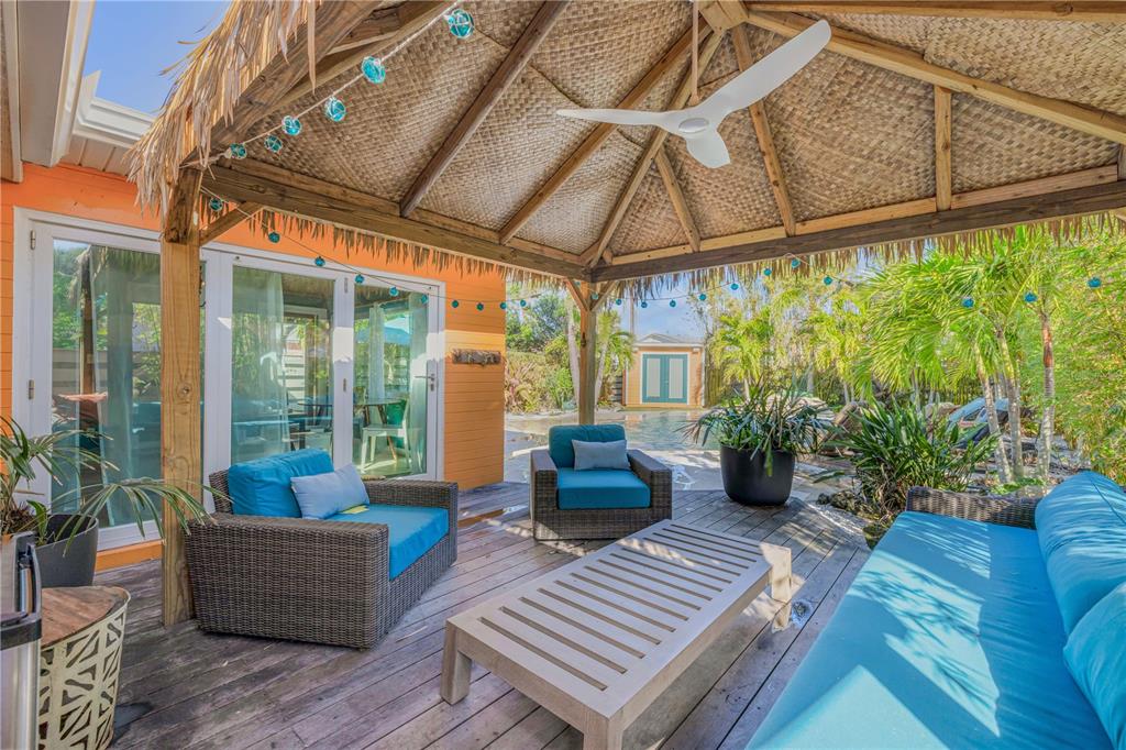 A covered wooden deck features a tiki-style roof, outdoor furniture, and a view of a pool — 308 NORMANDY AVENUE, NEW SMYRNA BEACH, FL