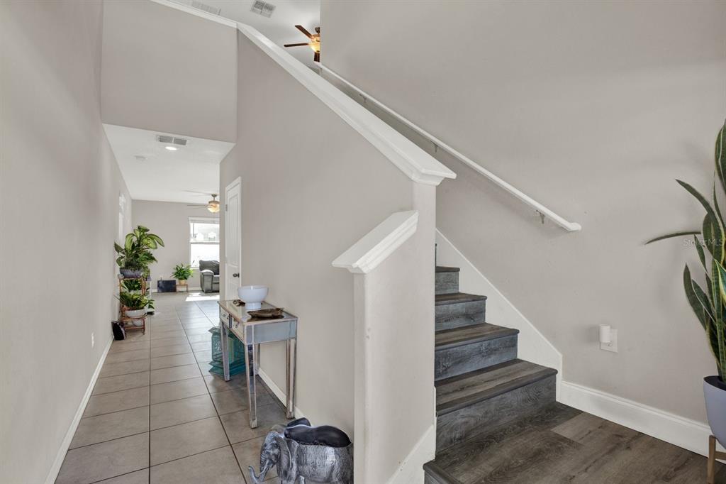 A staircase with dark wood treads sits beside a tiled hallway leading to a living area — 3707 DAISY BLOOM PLACE, TAMPA, FL