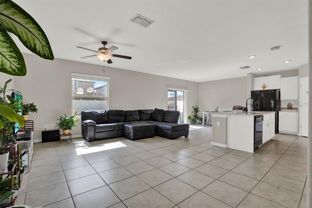 An open-concept living room and kitchen feature tile flooring, a sectional sofa, and white cabinetry — 3707 DAISY BLOOM PLACE, TAMPA, FL