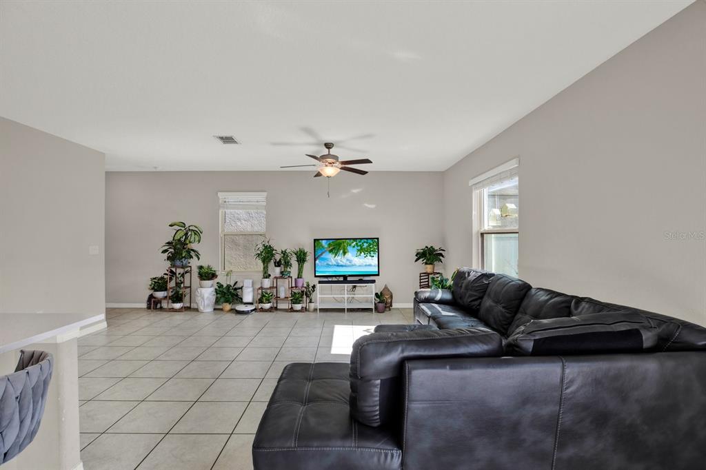 A living room features light tile flooring, a black leather sectional, and a television stand — 3707 DAISY BLOOM PLACE, TAMPA, FL