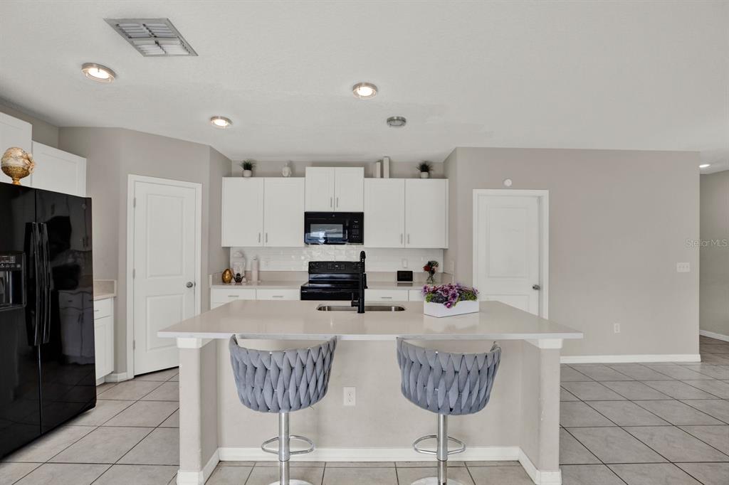A kitchen features white cabinets, black appliances, a central island with bar stools, and tile flooring — 3707 DAISY BLOOM PLACE, TAMPA, FL