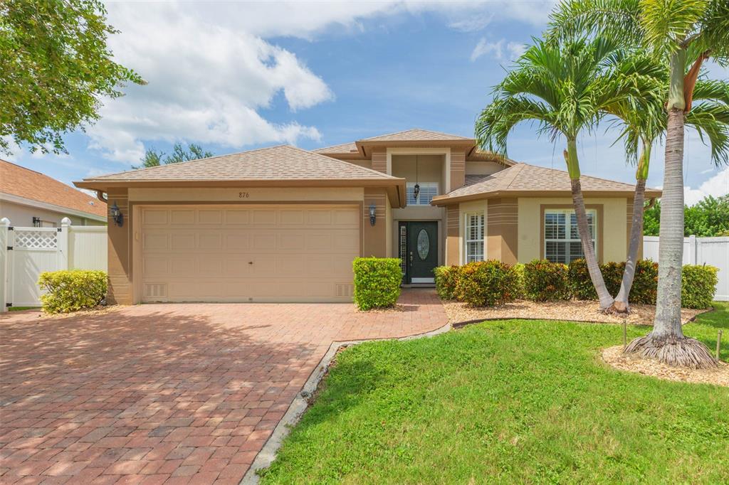 A tan single-story house with a brick driveway, palm trees, and a two-car garage — 876 ADDISON DRIVE NE, ST PETERSBURG, FL