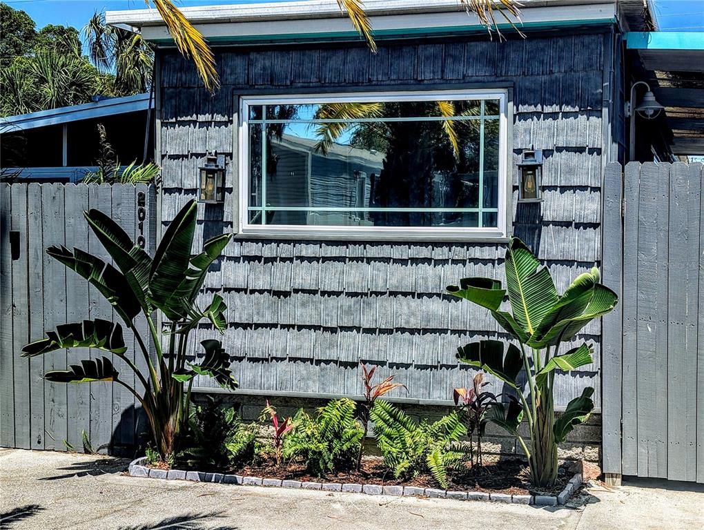 The exterior of a house features gray shingle siding, a large window, and tropical landscaping — 2010 KEPNER DRIVE, HOLIDAY, FL
