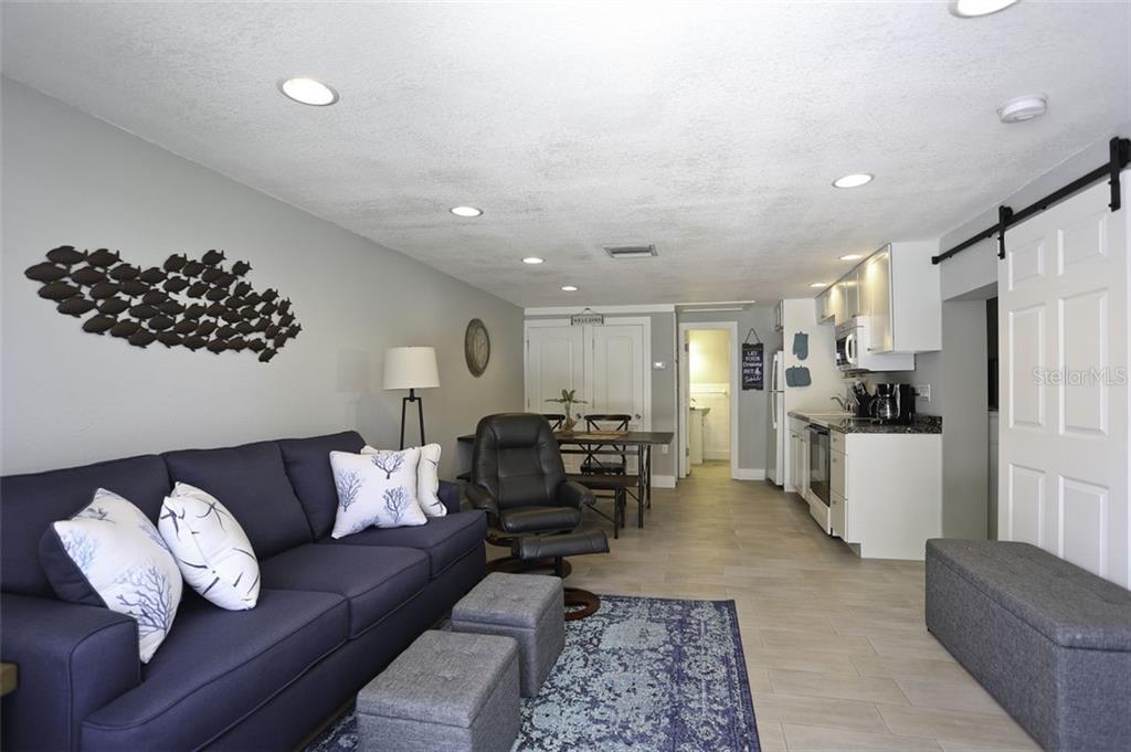 This open-concept living area features a blue sofa, a kitchen, and a dining table — 4621 103RD STREET W UNIT B, BRADENTON, FL
