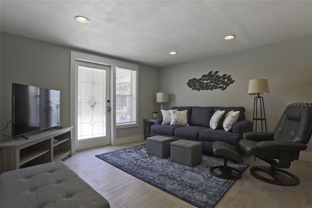 A living room features a dark sofa, a leather recliner, a patterned rug, and a glass-paneled door — 4621 103RD STREET W UNIT B, BRADENTON, FL