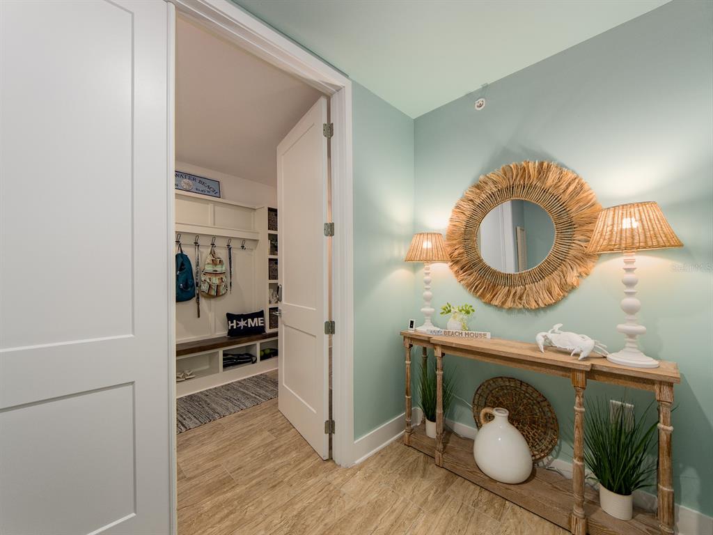 A hallway with a console table, round mirror, and an open doorway to a mudroom — 15 AVALON STREET UNIT 403, CLEARWATER BEACH, FL