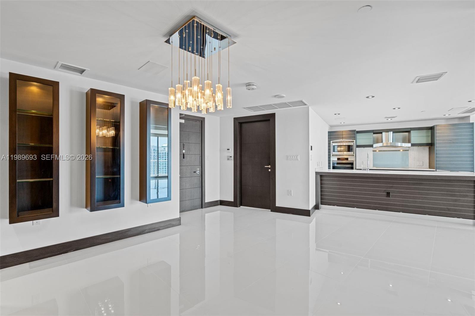 A modern, open-concept living area features white tile floors, dark wood cabinetry, and a crystal chandelier — 200 Biscayne Boulevard Way # 3707, Miami FL 33131, MIAMI, FL